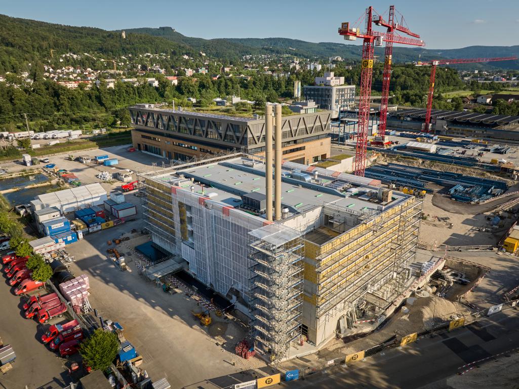 Vue aérienne du chantier UpTown Basel. L'image montre un grand bâtiment en construction, entouré d'échafaudages et de grues de construction.