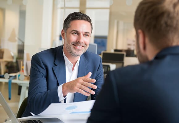 Deux hommes en conversation dans un bureau, l'homme de devant tient un document et sourit.
